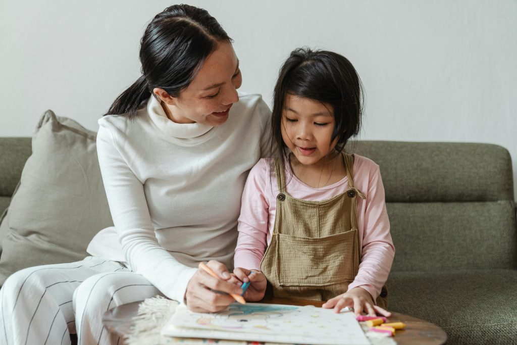 A mother helps her young daughter with a colorful drawing at home, fostering creativity and bonding.
