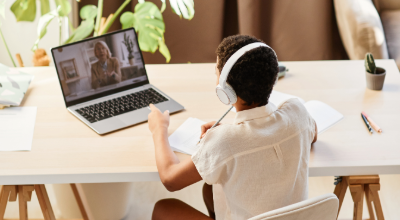 Student wearing headphones taking online classes on a laptop while studying at home.