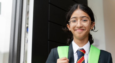 Confident student in school uniform with backpack smiling outside the classroom.